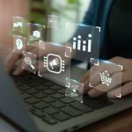 Person typing on laptop with digital icons for analytics, marketing, AI, and e-commerce floating above the keyboard.